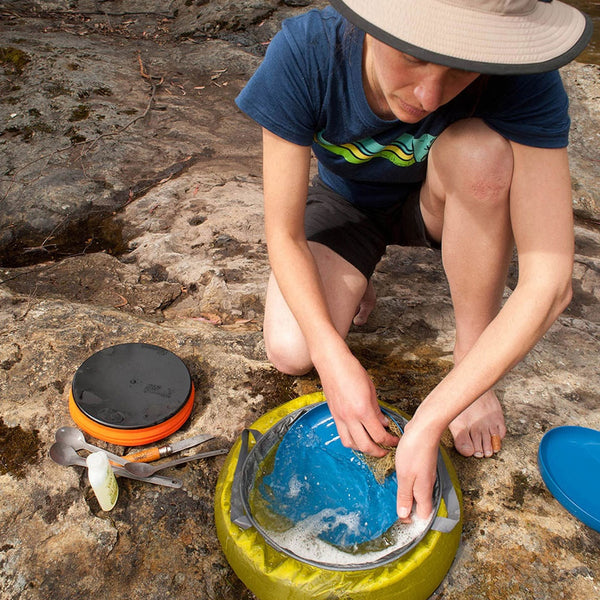 Lifestyle image of a person washing up their dinnerware after having a meal outdoors using a Sea To Summit ultra-sil collapsible kitchen sink